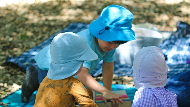 Young children in hats playing on picnic mats