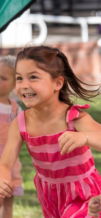 A young girl and boy running beneath a parachute.