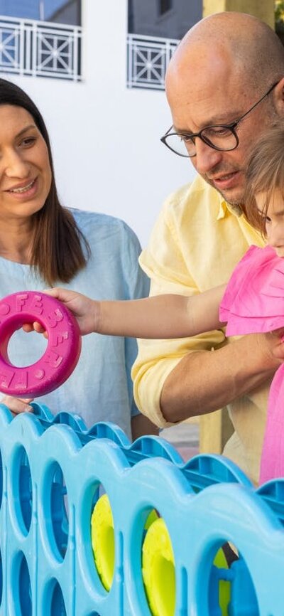 A father holding his young daughter while she places hoops into an oversized Tick-tack-toe game.