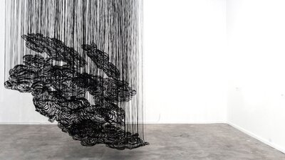 A black  artwork installation suspended from the ceiling of an art gallery.