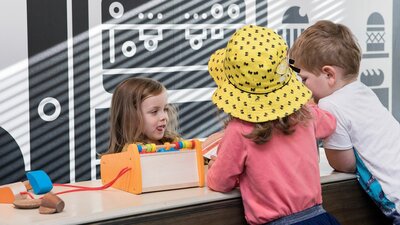 Three young children playing shop in the Kindness Café space