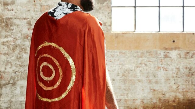 Dennis Golding with The Future is Here, 2021 A man stand away from camera with a red cape and gold circles painted on it