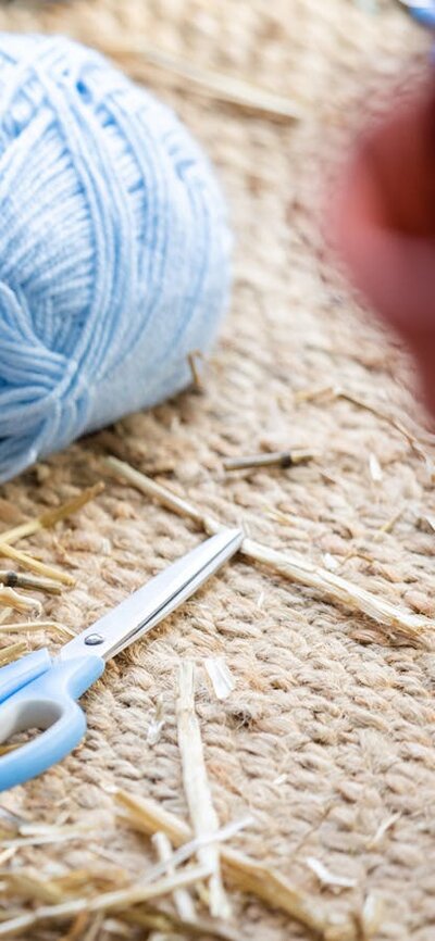 Person wrapping blue yarn around a bundle of straw