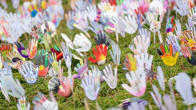 Colorful hand-shaped cutouts decorated with various patterns, mounted on sticks on grass area