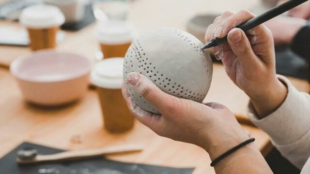 Reflective Clay Workshop Hands hold a clay sphere, poking holes in with a tool for decoration