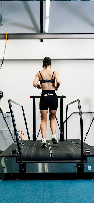 A woman in active wear runs on a treadmill for biomechanics testing with a researcher observing.