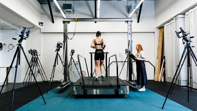 A woman in active wear runs on a treadmill for biomechanics testing with a researcher observing.