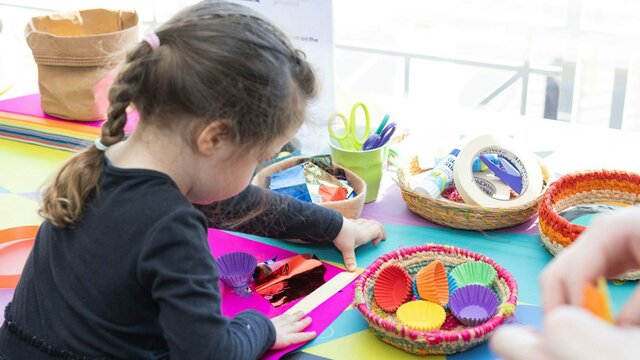 A young girl busy at a crafting table with colourful art supplies.
