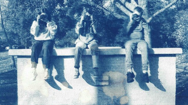 A cyanotype print photograph of three kids sitting on a ledge holding cameras up to their faces
