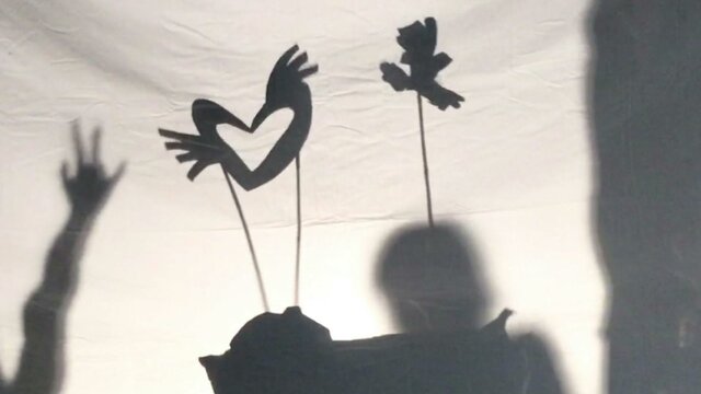 Shadow puppets move across a screen as the outlines of children dancing are visible on either side
