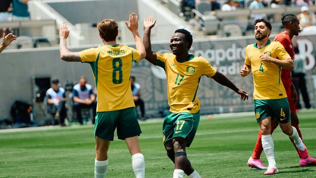 Soccer players in yellow kits celebrate a goal on a stadium pitch as teammates run in behind