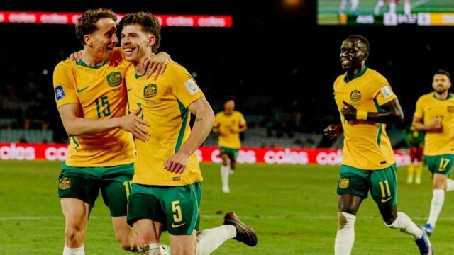 Soccer players in yellow kits celebrate a goal on a stadium pitch as teammates run in behind