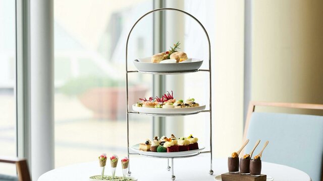 Three plates on high tea stand with two smaller dishes next to the stand.