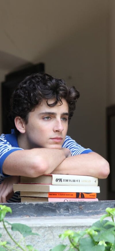 A teenage boy leans on some books and looks out of a window