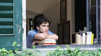 A teenage boy leans on some books and looks out of a window