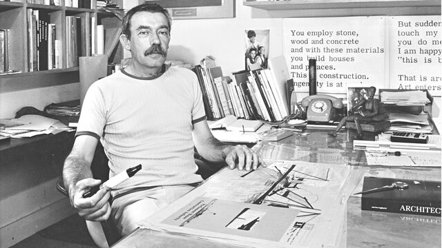 Enrico Taglietti in studio, 1985, photo by Ted Richards Enrico Taglietti holding a pen at his desk in his studio, photo taken in 1985