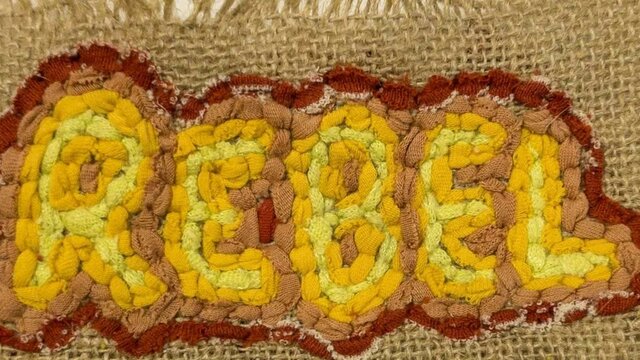 Henry Shawcross | Textile Works 2025 The word "Rebel" in yellow and red, made using the rag rugging technique