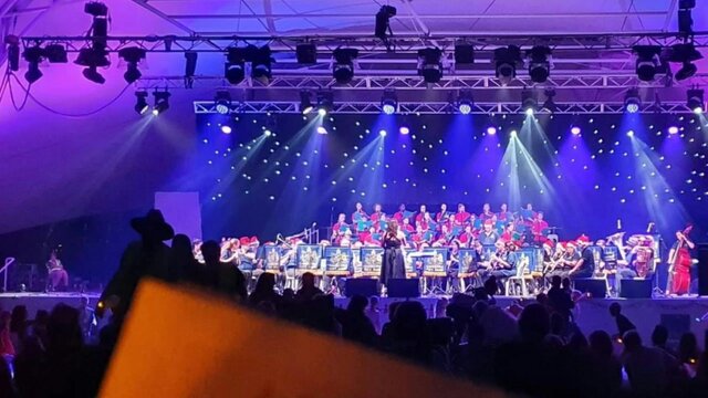 The Canberra Times Carols by Candlelight A choir performs on an outdoor stage illuminated by purple stage lights with candles in the audience