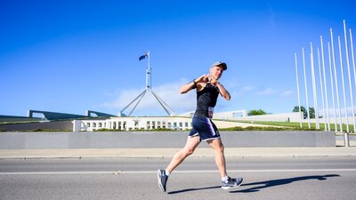 Man running past the Parliament House while doing the heart sign with his hands.