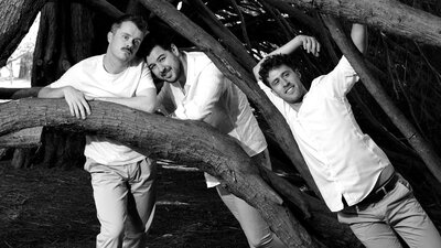 Three people standing amonst the branches of a tree in white clothing, looking at the camera