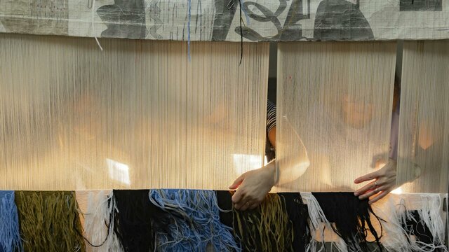 Courtesy the Manufactura de Tapeçarias de Portalegre The back of a tapestry being woven by people on the other side