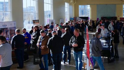 crowd of people inside a large, well lit warehouse tasting whiskies.