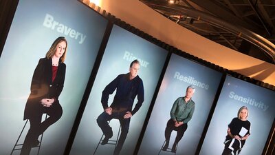 Four 7-foot tall video screens showing four journalists sitting on stools