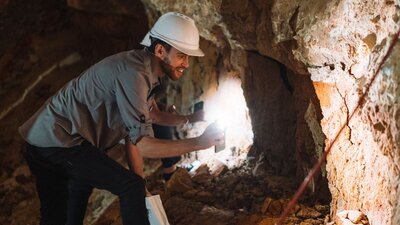 Person in a hard hat looking at a rock formation with a torch.