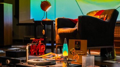 An armchair in front of a turntable and a lava lamp