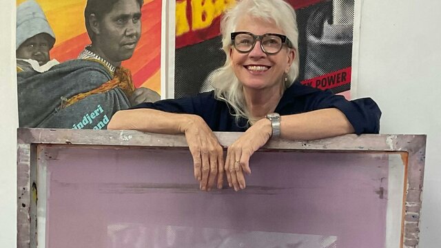 Alison Alder A woman with blonde hair and glasses leaning on a purple artwork piece.