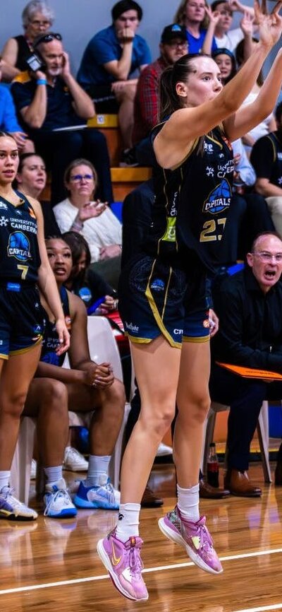 UC Capitals player Jayda Clark in the motion of shooting a 3 pointer with her teammates behind her.