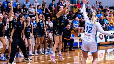 UC Capitals player Jayda Clark in the motion of shooting a 3 pointer with her teammates behind her.