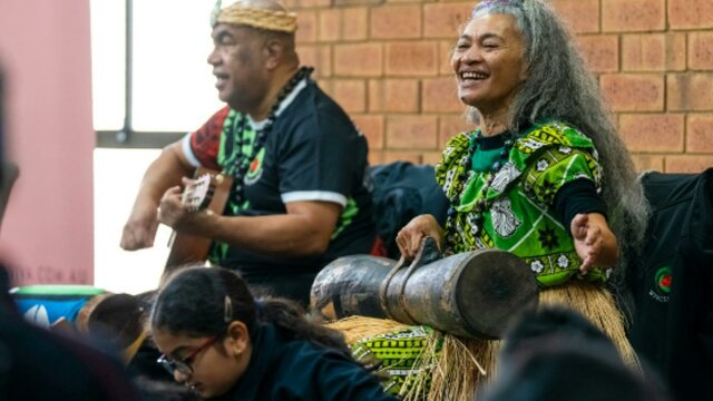 2 performers play music for an audience, one playing a guitar and one playing percussion instrument