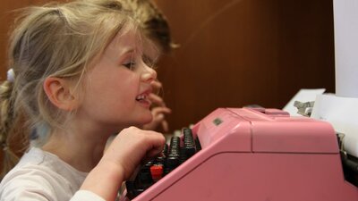 Girl smiling typing on a pink typewriter