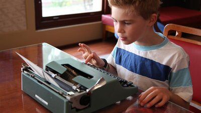 Boy carefully typing at an olive green typewriter