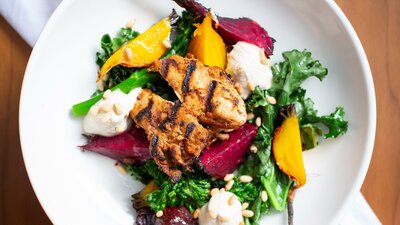 A colourful salad of broccolini, beats and chicken on a white plate.