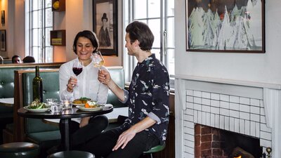 Couple with food and wine on tall stools by a fire place