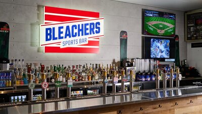 Lines of bottles along a bar with a bright sign in the background