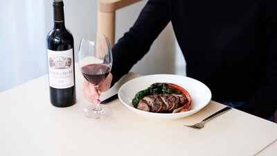 A guest holds a glass of red wine and food.