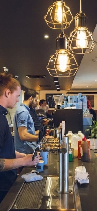 Wait staff serving drinks behind the bar with customers waiting to collect drinks