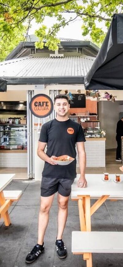 Two Cafe Cultura workers standing outside of the cafe, holding plates of food.