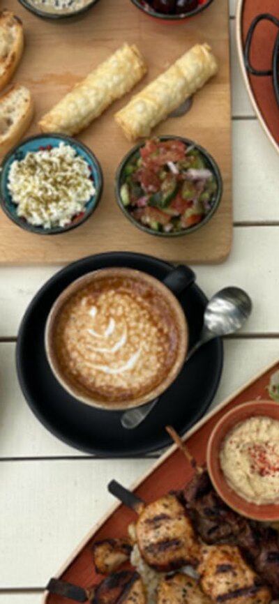 Array of Cafe Cultura offerings, including salad wraps and coffee, on white wooden table.