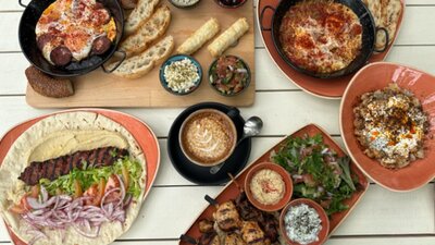 Array of Cafe Cultura offerings, including salad wraps and coffee, on white wooden table.