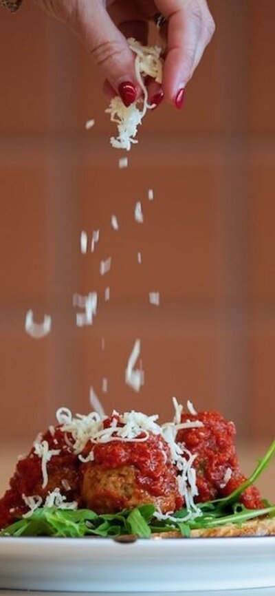 Plate of meatballs and spaghetti being topped with Parmesan cheese.