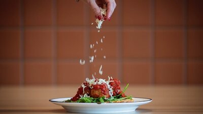 Plate of meatballs and spaghetti being topped with Parmesan cheese.