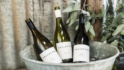 Three bottles of wine chill in a rustic bucket against a corrugated iron wall.