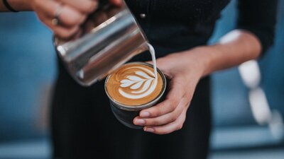 Barista wearing black pouring milk into a coffee cup