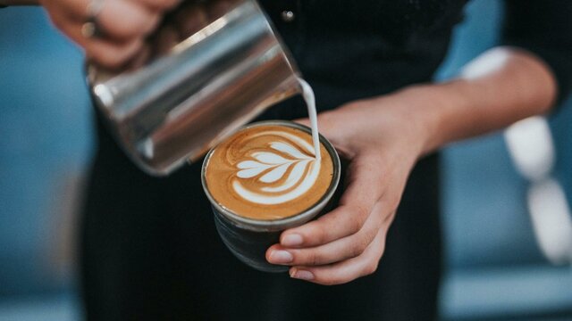 Barista wearing black pouring milk into a coffee cup