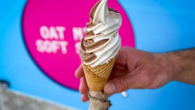 A hand holding a vanilla and chocolate soft serve icecream in a cone