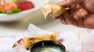 Hand holding a spring roll dipped in sauce